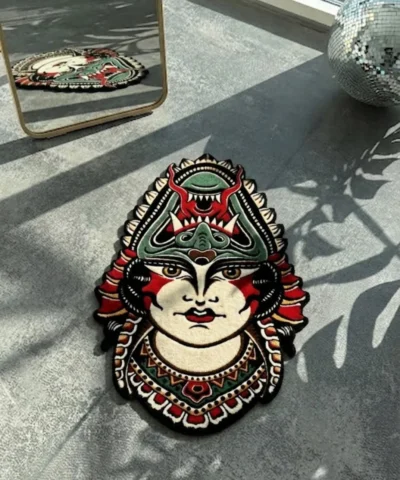 Top-down flat view of the die-cut Lady Face traditional tattoo rug, featuring a woman wearing a fierce green and red demon headdress, styled on a smooth concrete floor with striped sunlight shadows.