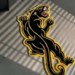 Wide perspective view of the hand-tufted Neo-Traditional Panther rug on a dark hardwood floor, beautifully showcasing the full crawling panther tattoo flash design in a cozy living space.