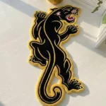 Top-down flat view of the rectangular Neo-Traditional Panther rug resting on a smooth concrete floor, featuring a dynamic black panther design with crisp white outlines and a red mouth, bathed in sharp, striped sunlight shadows.