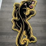 Close-up angled detail of the Neo-Traditional Panther rug on a dark wood floor, emphasizing the plush thickness of the black wool base and the clean, carved white lines defining the panther's curved tail and back claws.