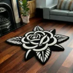 Perspective view of the Noir Rose black and white traditional tattoo rug styled on a dark wood floor in a living room next to a classic black fireplace, a potted plant, and a grey sofa.