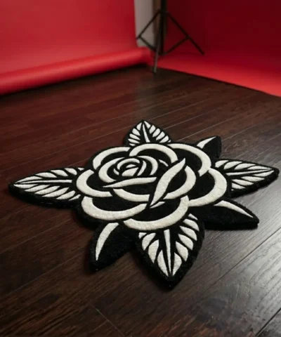 Angled view of the Noir Rose black and white flower rug placed on a dark wood floor in a photography studio setting, featuring a vibrant red seamless paper backdrop unrolled in the background.