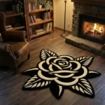 Wide perspective view of the Noir Rose black and white flower rug resting on dark hardwood floors in a warm den, surrounded by a wooden bookcase, a glowing floor lamp, a lit stone fireplace, and a brown leather armchair.
