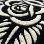 Close-up macro detail of the Noir Rose rug, highlighting the dense hand-tufted black wool pile and the thick, crisp white 3D carved lines that define the rose petals.