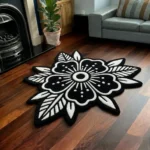 Perspective view of the Obsidian Bloom black and white traditional tattoo flower rug styled on a wooden floor in a living room next to a classic black fireplace, a potted plant, and a light grey sofa.
