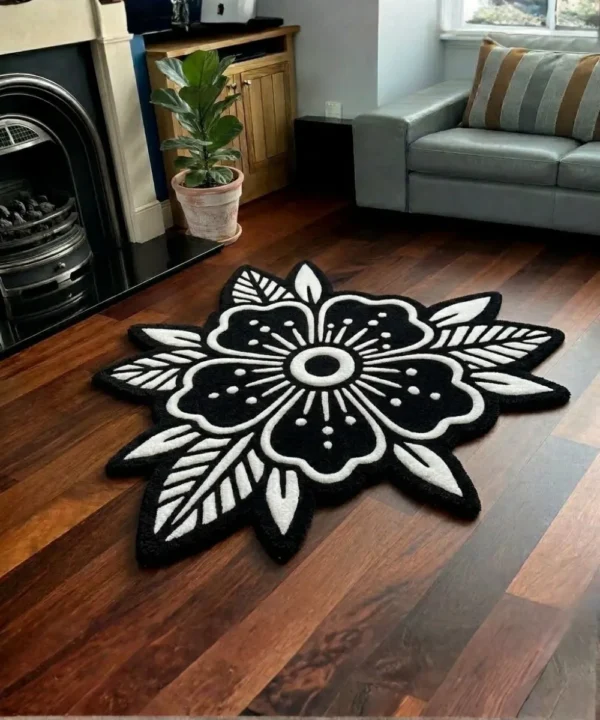 Perspective view of the Obsidian Bloom black and white traditional tattoo flower rug styled on a wooden floor in a living room next to a classic black fireplace, a potted plant, and a light grey sofa.