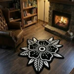 Wide perspective view of the Obsidian Bloom black and white flower rug styled in a warm library or den, surrounded by a wooden bookcase, a glowing floor lamp, a lit stone fireplace, and a classic brown leather wingback chair.