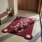 Perspective view of the burgundy Panther of Hearts rug styled in a sunlit, modern entryway on a smooth light concrete floor, placed near a warm wooden bench and doorway.