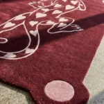 Close-up angled detail of the Panther of Hearts rug basking in sunlight, highlighting the dense hand-tufted wool pile, a pink circular corner, and the crisp 3D carving of the pink hearts and panther outline.
