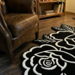 Angled perspective view of the Petal Duet twin rose tattoo flash rug styled on a dark wooden floor right next to a classic brown leather wingback chair.
