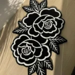 Top-down angled view of the Petal Duet black and white traditional tattoo rose rug bathed in striking natural sunlight and shadows on a light wooden floor.