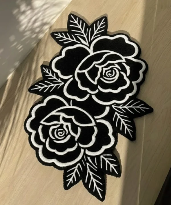 Top-down angled view of the Petal Duet black and white traditional tattoo rose rug bathed in striking natural sunlight and shadows on a light wooden floor.
