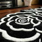 Low-angle close-up view of the Petal Duet rug near a fireplace hearth, highlighting the plush thickness of the hand-tufted wool and the deep 3D carving of the crisp white outlines against the solid black background.