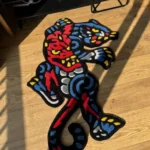 Angled perspective view of the vibrant Phantom Panther neo-traditional tattoo rug, perfectly showcasing its dynamic shape, sharp claws, and striking red and blue color palette on a warm hardwood floor.