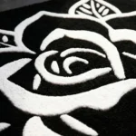 Close-up macro detail of the Phantom Rose rug, highlighting the dense hand-tufted black wool base and the deep, crisp carving of the bold white traditional tattoo rose lines.