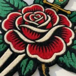 Close-up angled detail of the edge of the Rose and Dagger rug bathed in natural light, showcasing the plush thickness of the hand-tufted pile and the clean, carved lines defining the green leaves.