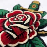 Close-up macro detail of the Rose and Dagger rug, highlighting the totally dense hand-tufted texture and the deep carving of the dagger's ornate hilt.