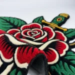 Angled perspective view of the Rose and Dagger rug, emphasizing the thick 100% New Zealand wool pile and the crisp 3D carving that separates the sharp dagger from the soft rose petals.