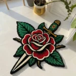 Top-down flat view of the Rose and Dagger rug, showcasing its bold American traditional tattoo flash design featuring a vibrant red rose pierced by a classic silver and gold dagger.