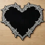 Top-down view of the Sacred Heart rug on a light wood floor, featuring a solid black heart shape boldly outlined by a thick, white traditional tattoo barbed wire border.