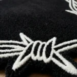 Close-up macro detail of the Sacred Heart rug, highlighting the dense black hand-tufted wool pile and the crisp carving of the white barbed wire motif.