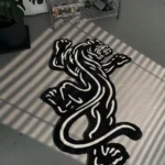 Angled close-up view of the Black Veil black and white rose rug placed on a smooth grey concrete floor, beautifully illuminated by dramatic slatted window blind shadows.