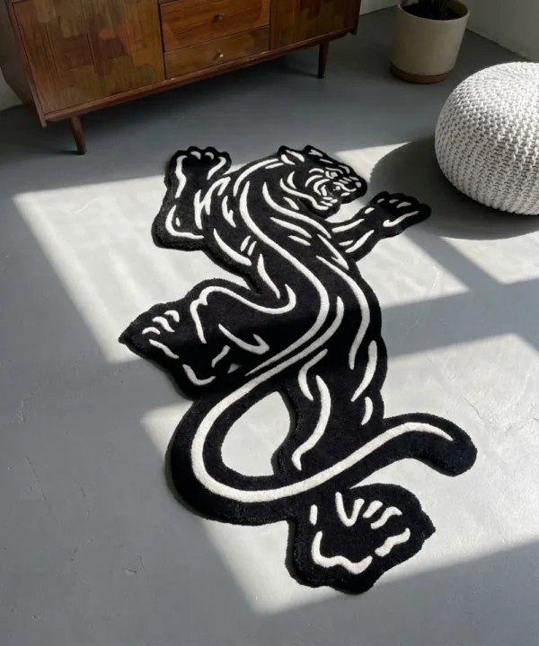 Perspective view of the Black Veil black and white traditional tattoo rose rug styled on a wooden floor in a living room next to a classic black fireplace, a potted plant, and a light grey leather sofa.