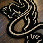 Top-down view of the Black Veil rose-shaped rug resting on a concrete floor with striking window blind shadows cast across its surface, emphasizing the bold contrast of the white carved lines on the black wool background.