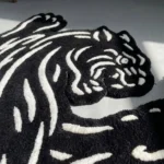 Close-up angled view of the Black Veil rose rug resting on a dark hardwood floor, highlighting the thick hand-tufted wool pile and the crisp 3D carving of the white floral outlines against the solid black base.