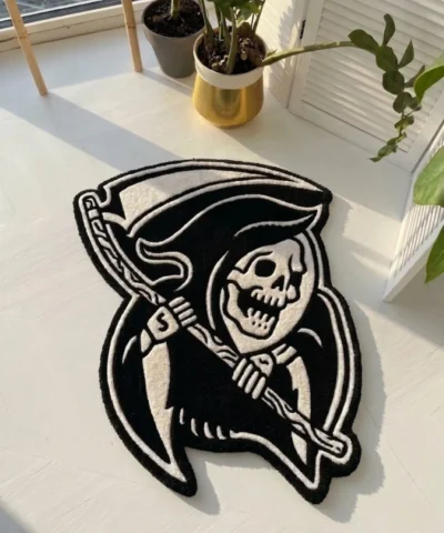 Angled perspective view of the Shadow Reaper black and white traditional tattoo flash rug resting on a white wooden floor, bathed in bright natural sunlight.