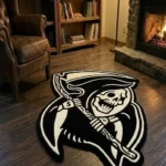 Wide perspective view of the Shadow Reaper black and white grim reaper rug styled on a dark hardwood floor in a warm den, featuring a lit stone fireplace, a wooden bookcase, and a classic brown leather armchair.