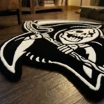 Low-angle close-up view of the Shadow Reaper rug resting on a dark wood floor near a fireplace hearth, emphasizing the plush, thick edge of the hand-tufted wool pile.