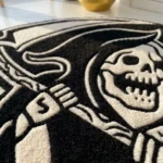 Low-angle close-up view of the Shadow Reaper rug, showcasing the plush thickness of the hand-tufted wool and the deep carving of the stark white skeletal teeth and hood against the solid black background.