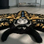 Low-angle close-up view of the Skull Death Moth rug, shot from the top antennae looking down the center, emphasizing the thick, plush hand-tufted New Zealand wool pile, the stylized white skull, and the blue dotted abdomen.