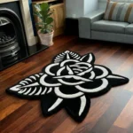 Perspective view of the Thornveil black and white traditional tattoo rose rug styled on a wooden floor in a living room next to a classic fireplace and a light grey sofa.