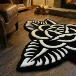 Angled view of the Thornveil black and white rose shaped rug resting on dark hardwood floors in a cozy room with a lit stone fireplace, firewood, and a brown leather armchair.