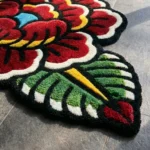 Angled close-up detail of the Traditional Peony rug, emphasizing the plush thickness of the hand-tufted wool and the crisp carved lines cleanly separating the bright green leaves and pink petals.