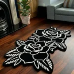 Perspective view of the Twin Ink Rose black and white double flower tattoo rug styled on a dark wood floor in a living room next to a potted plant, a black fireplace, and a light grey sofa.