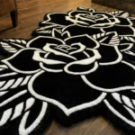 Angled perspective view of the Twin Ink Rose rug resting on dark hardwood floors in a warm, cozy den near a lit stone fireplace and the leg of a brown leather chair.