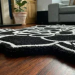 Low-angle close-up view of the Twin Ink Rose rug on a dark hardwood floor, showcasing the plush thickness of the hand-tufted wool and the deep carving along the outer edges of the black and white design.