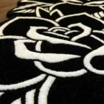 Close-up macro detail of the Twin Ink Rose rug, highlighting the dense hand-tufted black wool pile and the crisp white 3D carved lines that clearly outline the overlapping traditional rose petals.