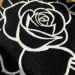 Top-down close-up view of the Void Blossom rug bathed in natural sunlight, emphasizing the stark contrast between the solid black wool background and the bright white carved floral outlines.