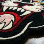 Close-up angled detail of the Wild Heart Panther rug, showcasing the plush texture and carved details of the yellow and blue eyes, white snout, and bold red hearts against the black wool base.