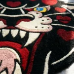 Extreme close-up side angle of the Wild Heart Panther rug bathed in natural sunlight, emphasizing the thick, totally dense texture of the hand-tufted wool and deep carving around the red hearts.