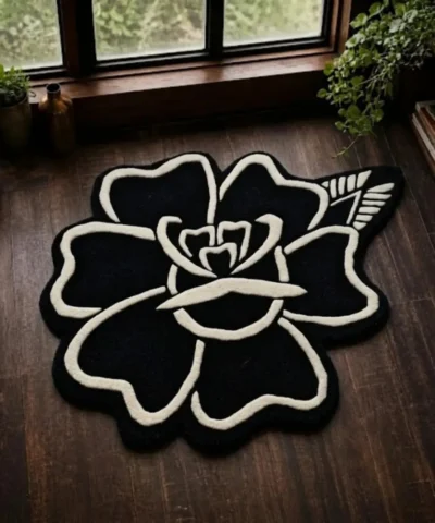 A full top-down product photograph of the Flash Rose rug on a dark wood floor, showcasing the bold black-and-white tattoo-inspired rose design in a distinct organic silhouette.