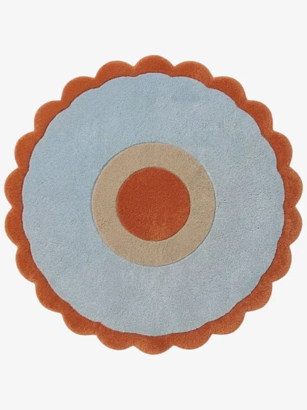 Top-down view of the Aurora Ring round rug, featuring a rust orange center circle, a cream middle ring, a wide light blue outer field, and a rust orange scalloped border.