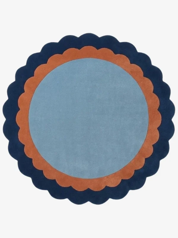 Top-down view of the circular Azure Halo rug featuring a light blue center framed by a double scalloped border in warm terracotta and deep navy blue.