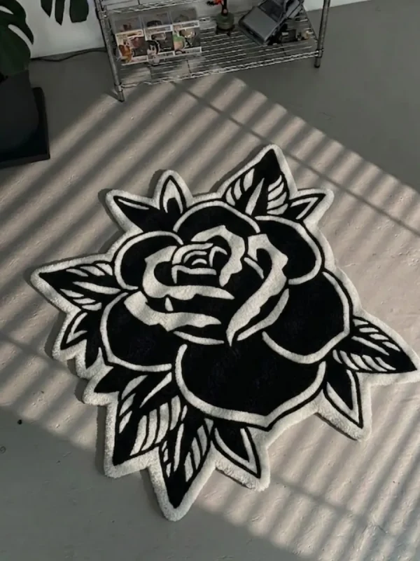 Top-down view of the Black Veil rose-shaped rug resting on a concrete floor with striking window blind shadows cast across its surface, emphasizing the bold contrast of the white carved lines on the black wool background.