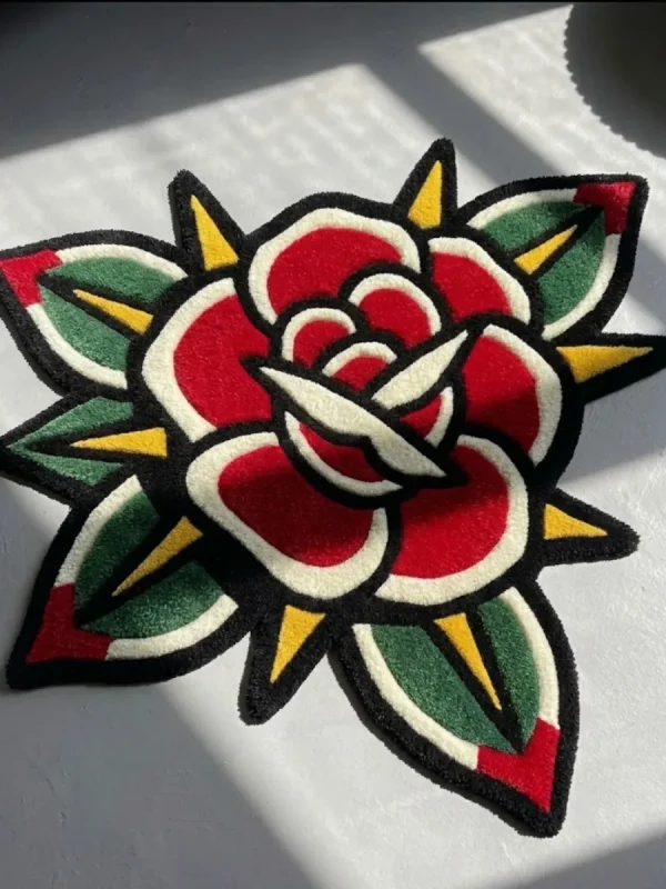 Top-down close-up view of the Classic Rose Tattoo Rug, emphasizing the bold traditional American tattoo flash style, red petals, and green leaf details in natural light.