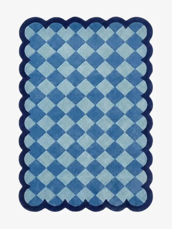 Top down view of the Coastal Current rug featuring a diamond checkerboard pattern in soothing shades of light and slate blue, framed by a dark blue scalloped border.